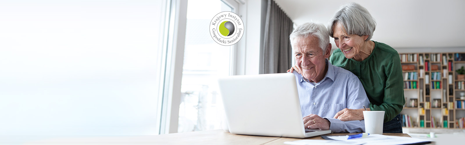 Para seniorów używa laptopa. Logo: Krajowy Instytut Gospodarki Senioralnej
