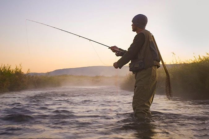 wędkarz o wschodzie słońca łowi ryby stojąc w jeziorze