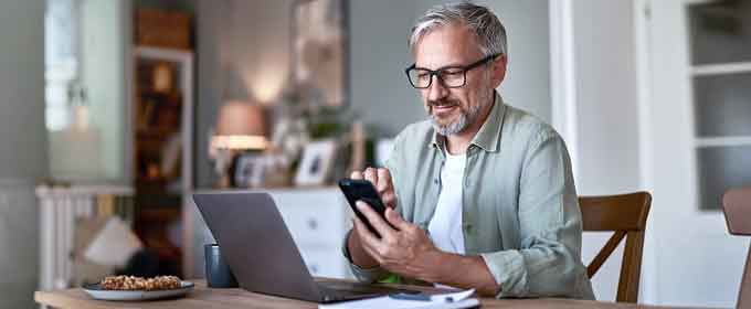 mężczyzna siedzi przy laptopie i patrzy w telefon