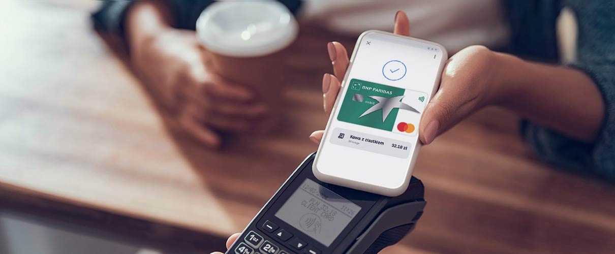 damska ręka płaci kartą w telefonie za kawę w kawiarni