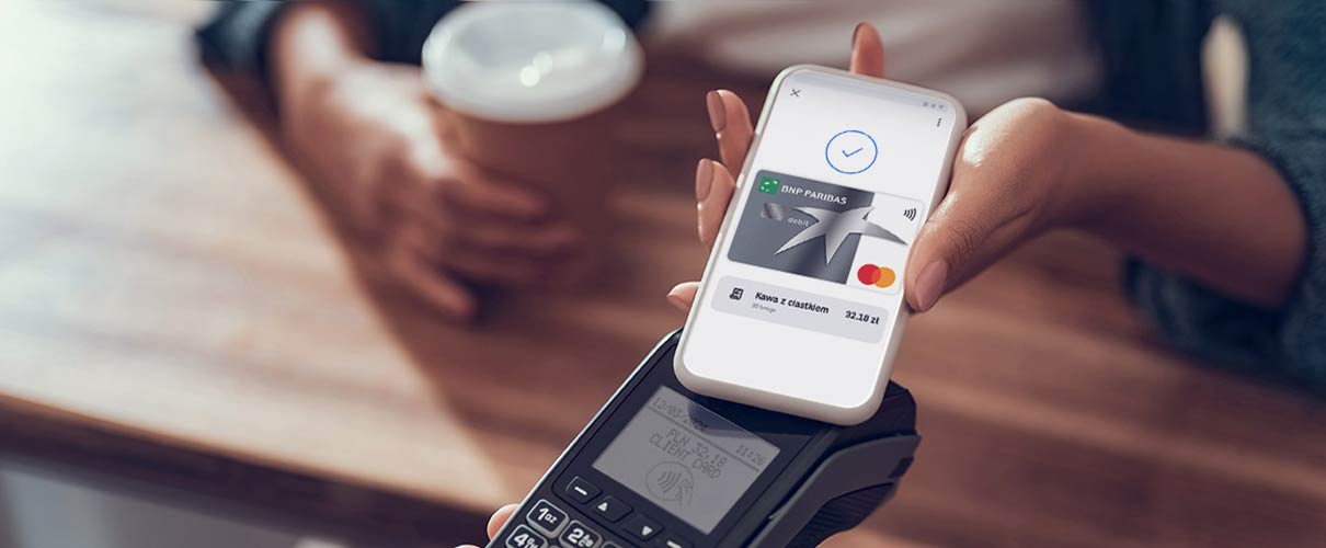 damska ręka płaci kartą w telefonie za kawę w kawiarni