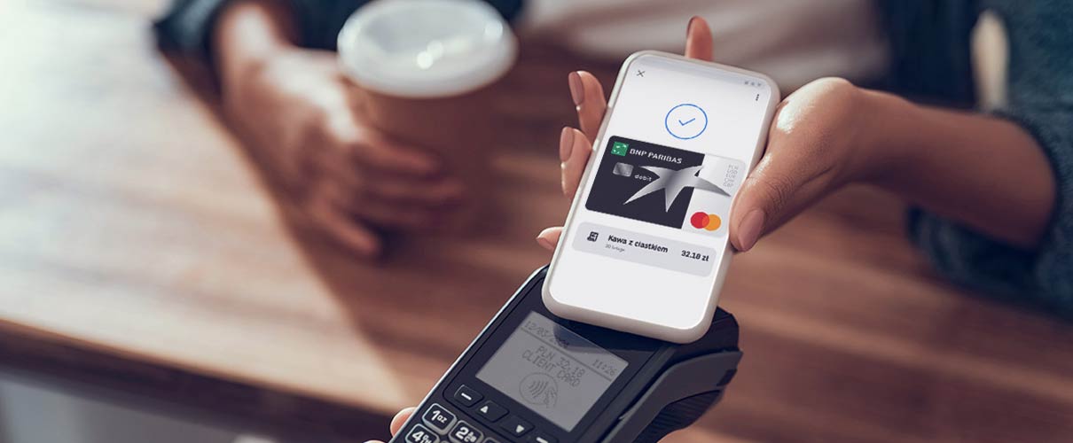 damska ręka płaci kartą w telefonie za kawę w kawiarni