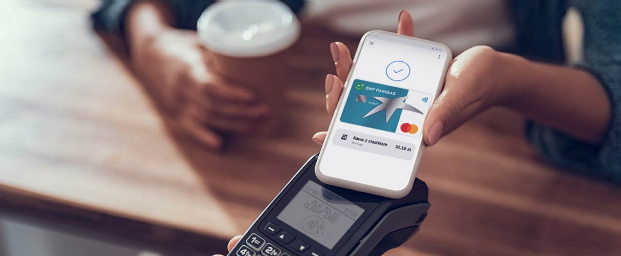 damska ręka płaci kartą w telefonie za kawę w kawiarni