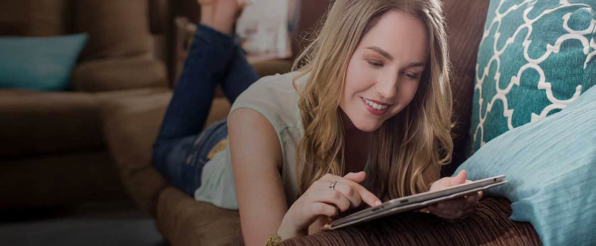 Pani leży na sofie i pracuje na tablecie