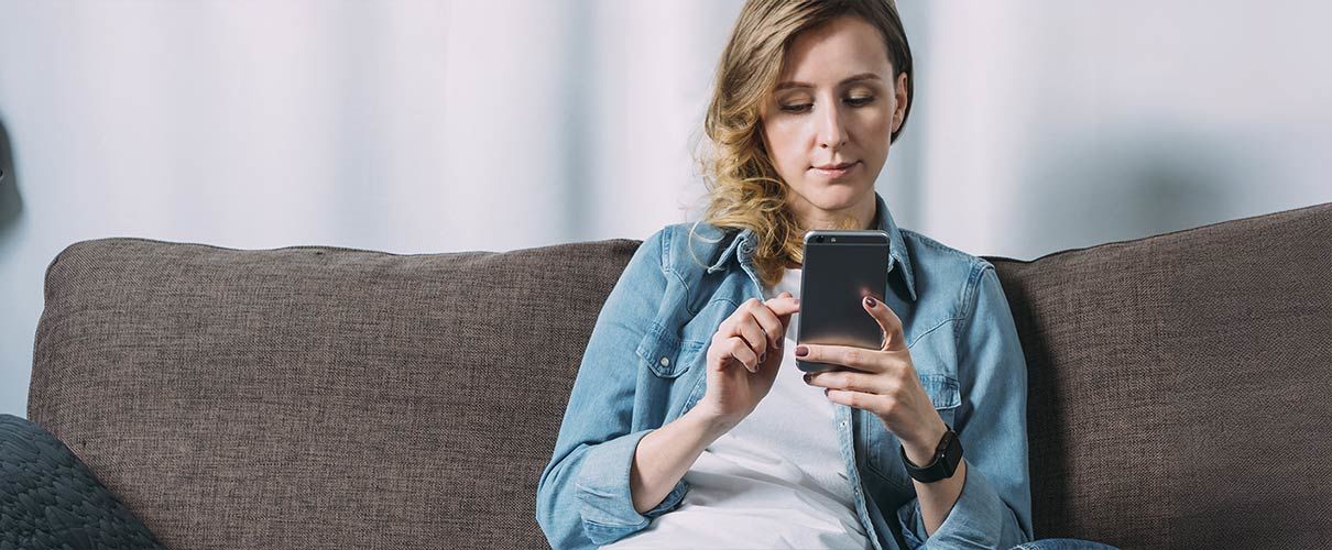 Pani siedzi na kanapie i patrzy na telefon komórkowy