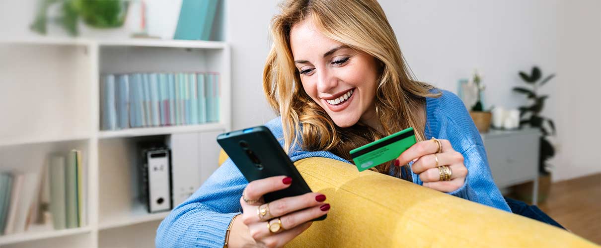 uśmiechnięta kobieta patrzy na telefon trzymając w ręku kartę