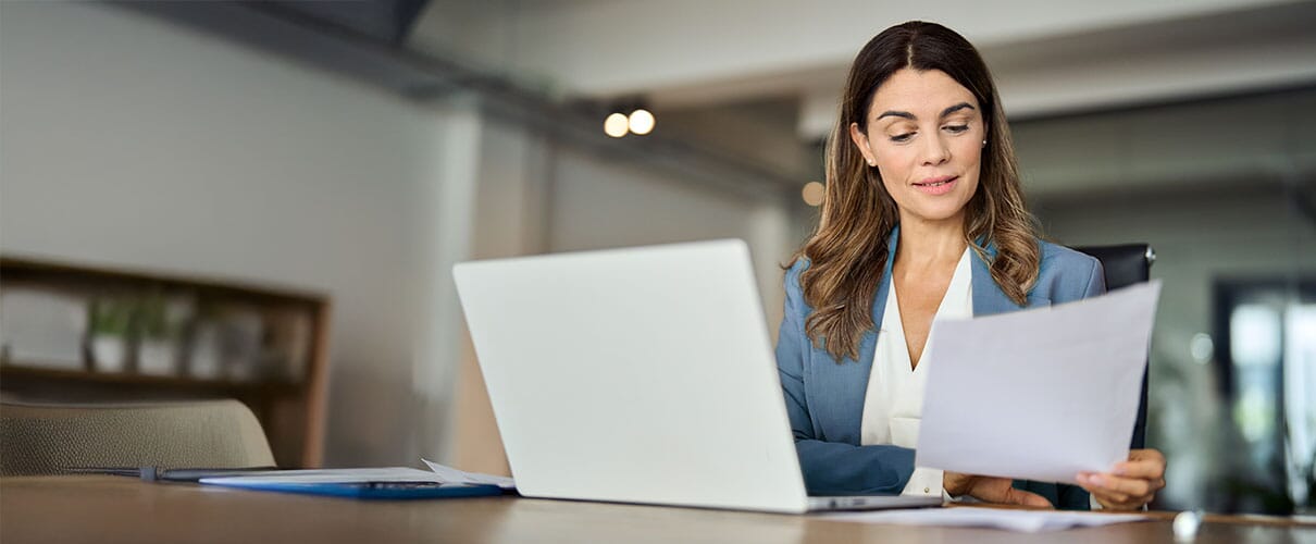 kobieta w koszuli i marynarce przegląda dokumenty przy biurku