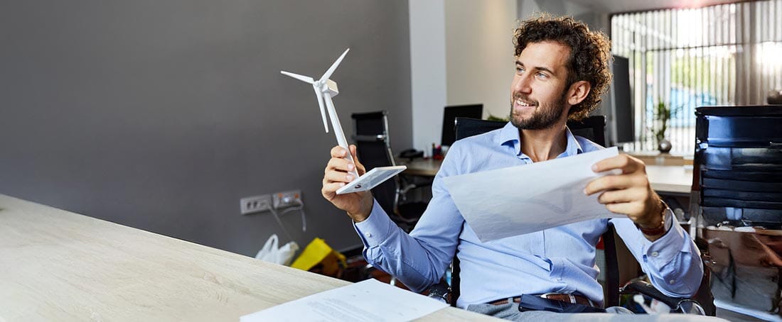 mężczyzna w koszuli siedząc na krześle w biurze trzyma dokument oraz mały wiatrak