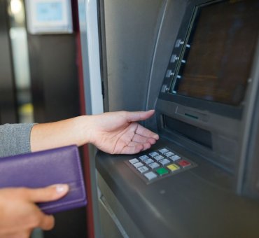 kobieta przy bankomacie, czekająca na kartę płatniczą