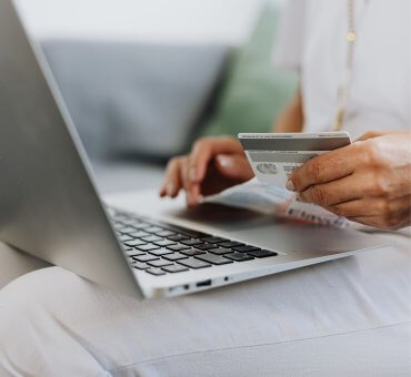 kobieta z laptopem i kartą bankową, czytająca o różnicach między kredytem a pożyczką