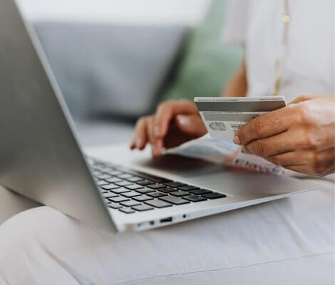 kobieta z laptopem i kartą bankową, czytająca o różnicach między kredytem a pożyczką