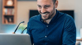 Mężczyzna w granatowej koszuli siedzący przed laptopem.