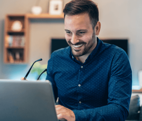 Mężczyzna w granatowej koszuli siedzący przed laptopem.