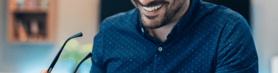 Mężczyzna w granatowej koszuli siedzący przed laptopem.