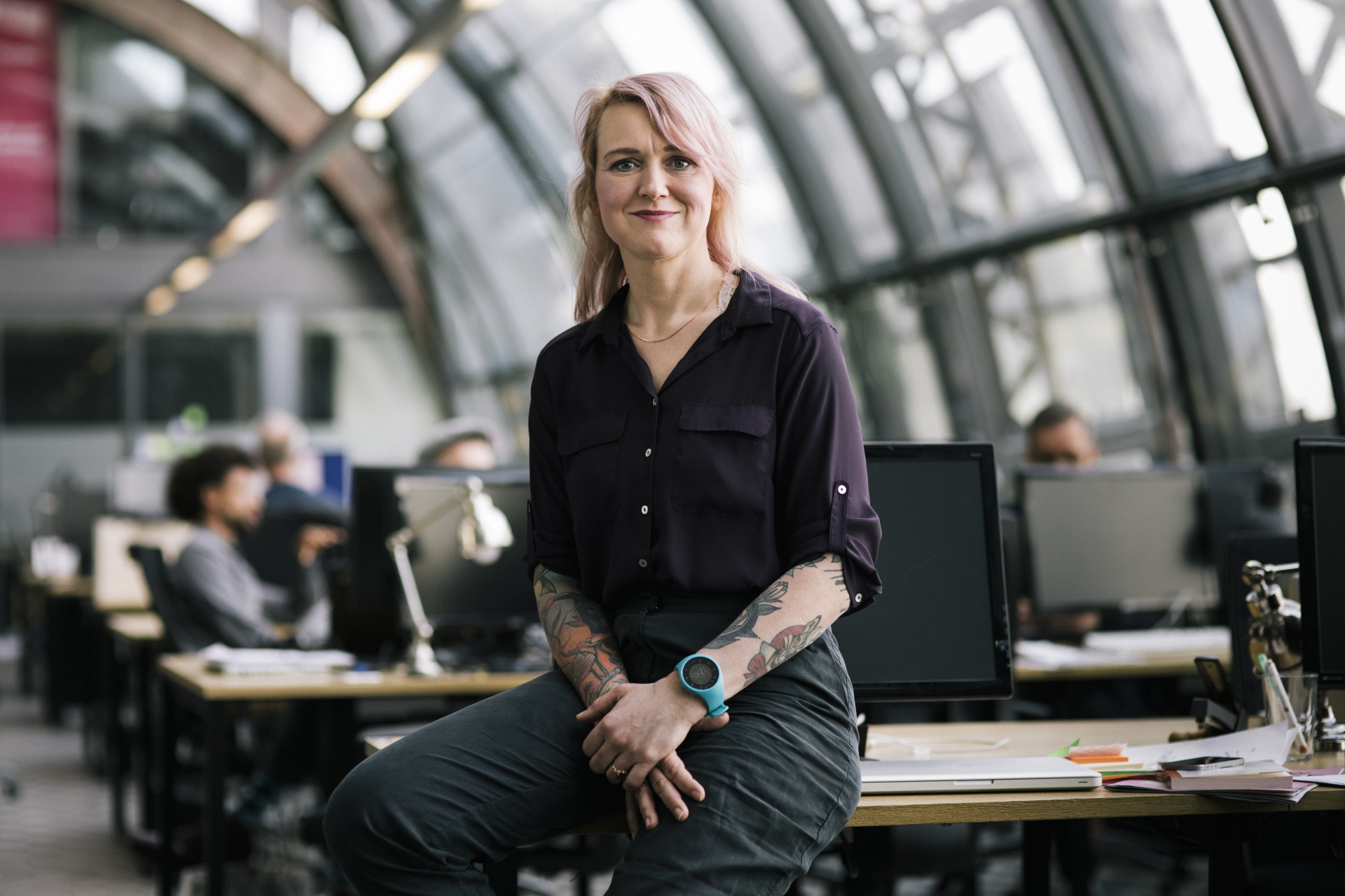 Uśmiechnięta dziewczyna z tatuażami siedząca przy biurku.