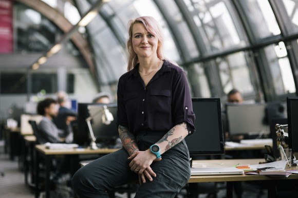 Uśmiechnięta dziewczyna z tatuażami siedząca przy biurku.