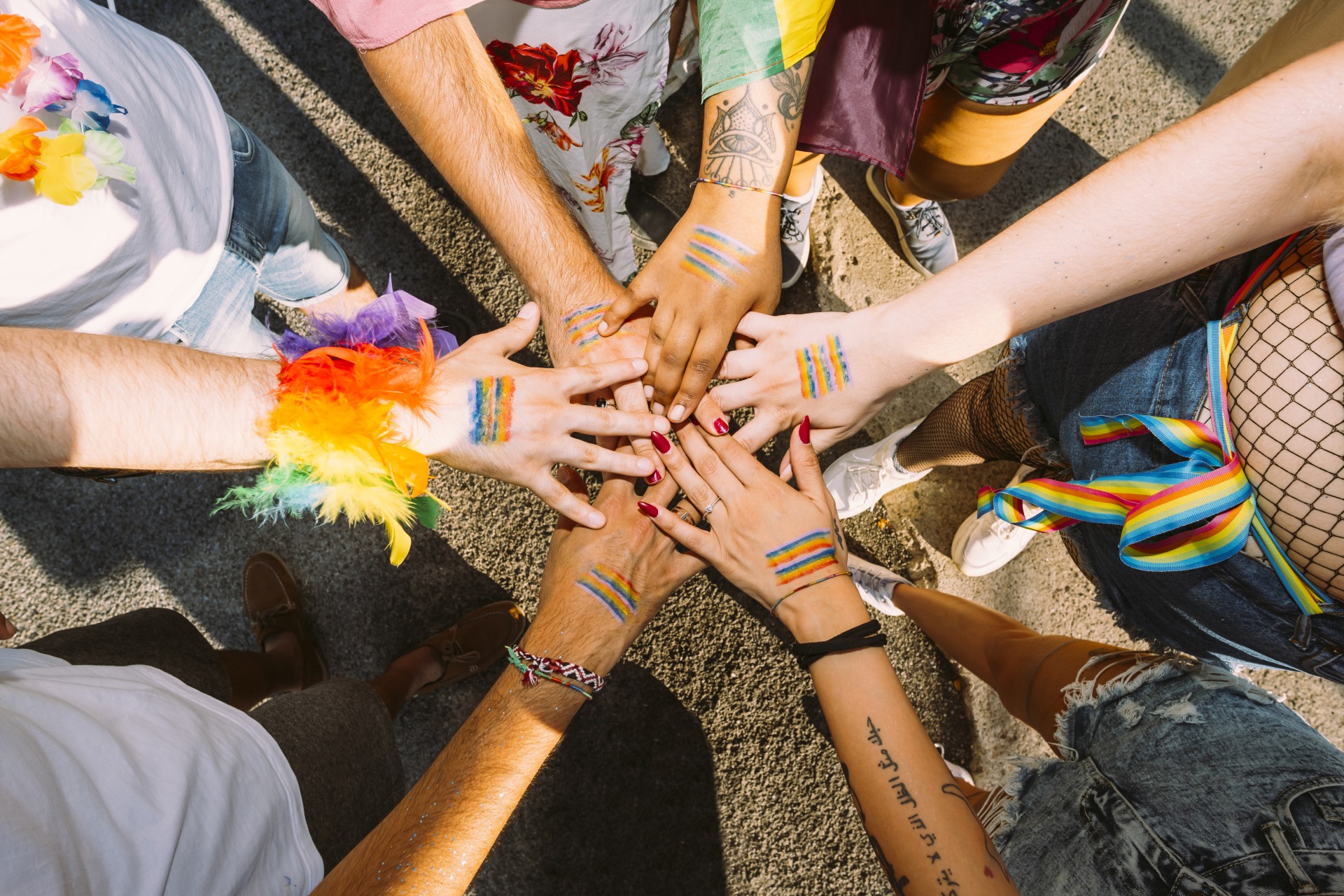 Grupa osób z symbolami tęczowymi na rękach pokazują współpracę.